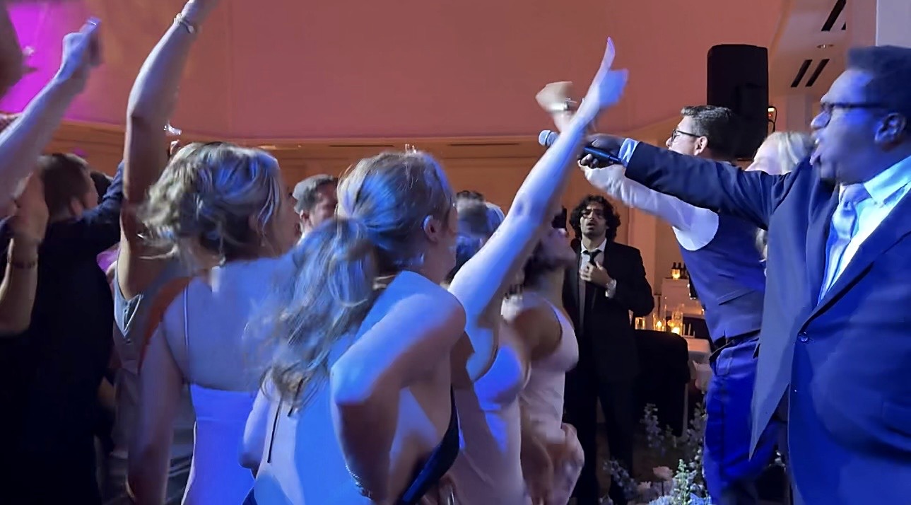 Gordon Dukes holding the microphone out to guests singing with raised arms on the dance floor