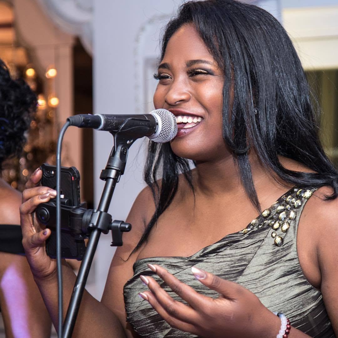Gabrielle-Nicole Dukes singing at a microphone stand, smiling mid-phrase