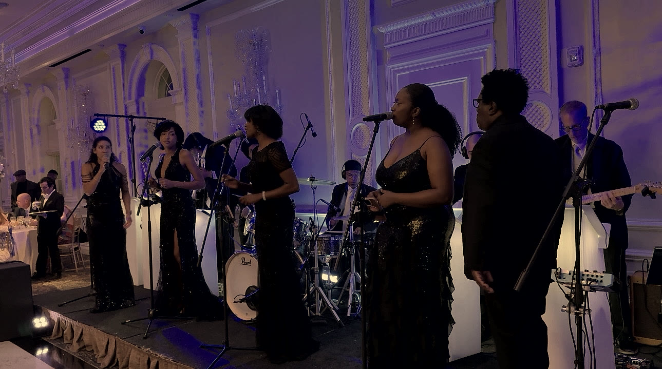 The Best Wedding Band's full ensemble — four vocalists, rhythm section and guitar — performing across a ballroom stage