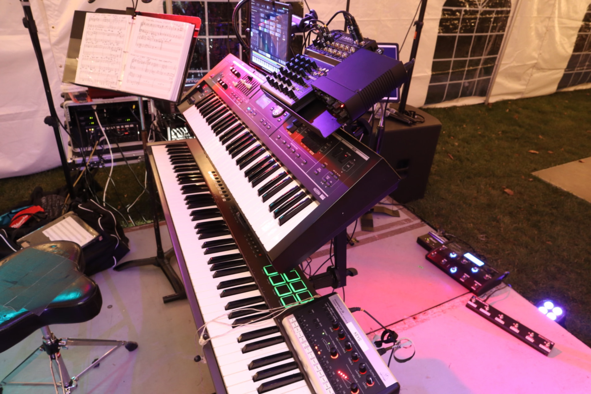 A Gordon Dukes Music Company keyboard rig under stage light — stacked keyboards, chart book and pedals set before the downbeat