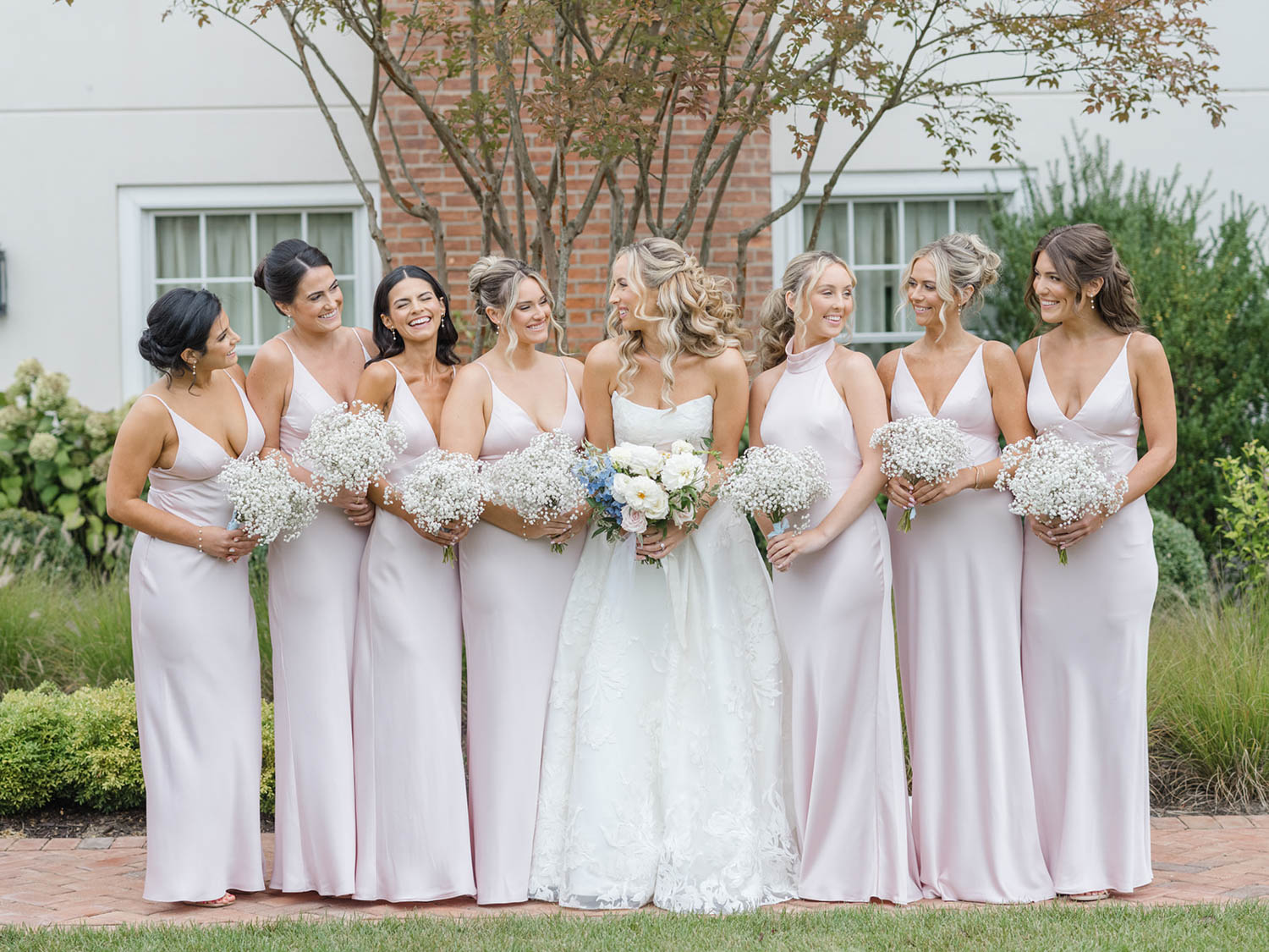 The bride surrounded by bridesmaids in blush satin holding bouquets