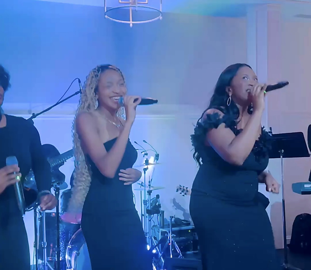 Two Gordon Dukes Music Company vocalists performing under blue stage light with the band behind them