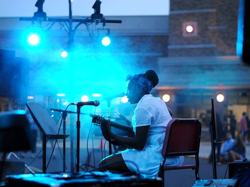 Gabrielle Dukes seated on stage singing into a microphone while playing guitar during a live performance — Gordon Dukes Music Company