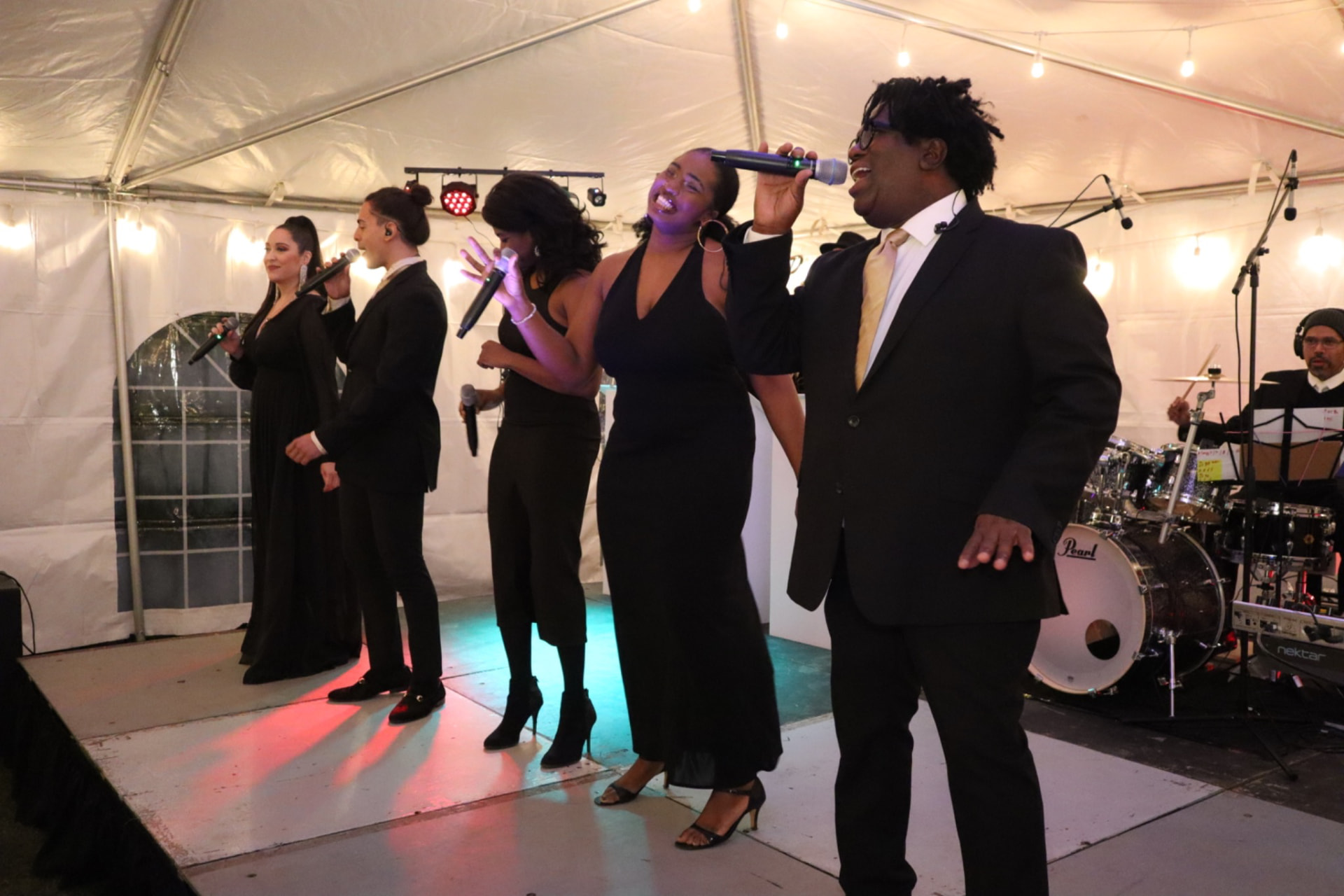 Gordon Dukes performing with the Gordon Dukes Music Company vocalists on a tented stage at a private celebration