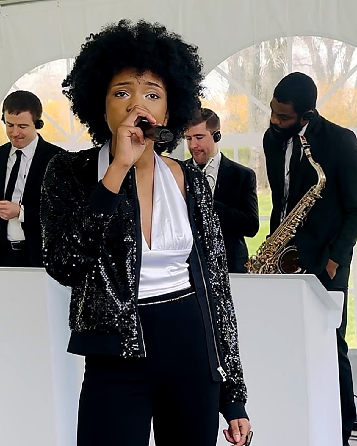 Saharrah Dukes of Gordon Dukes Music Company singing into a handheld microphone under a tent, band behind her