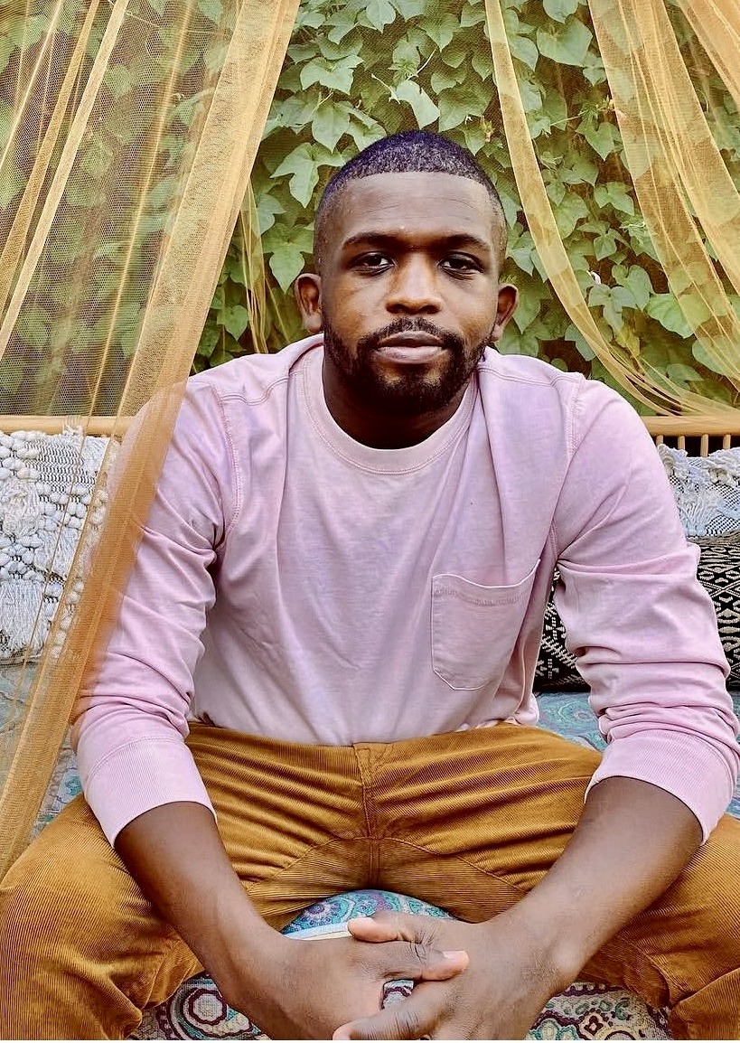 Donovan Dukes of Gordon Dukes Music Company seated beneath a gold curtain and greenery, hands clasped