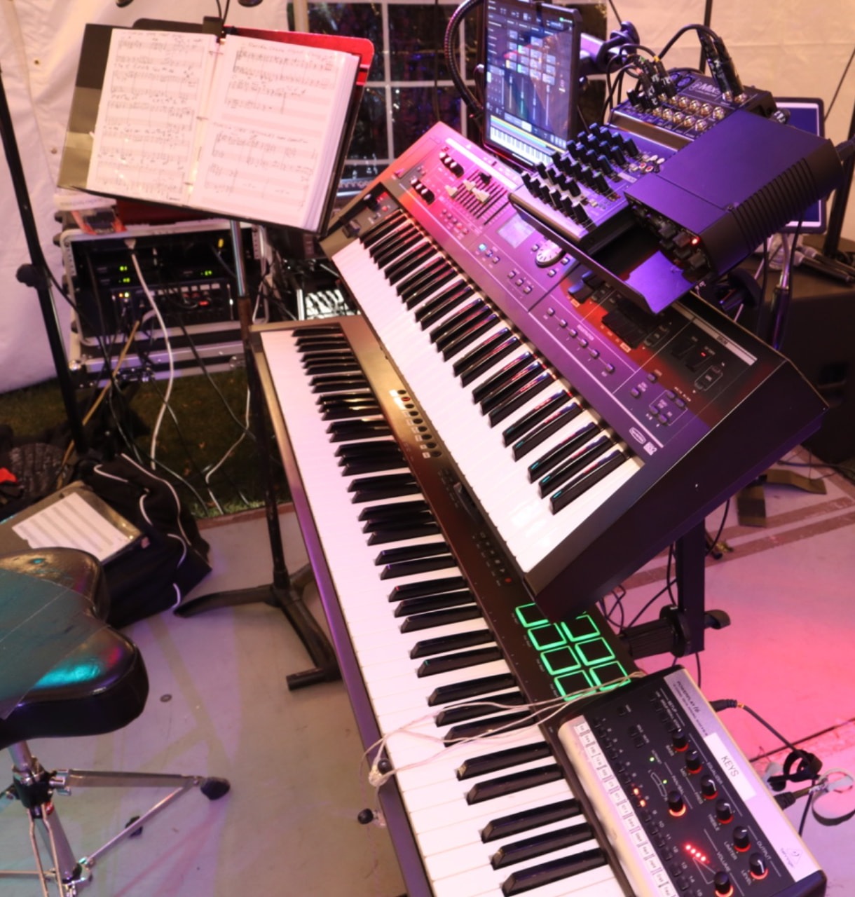 A Gordon Dukes Music Company keyboard rig under stage light — stacked keyboards, chart book and pedals set before the downbeat